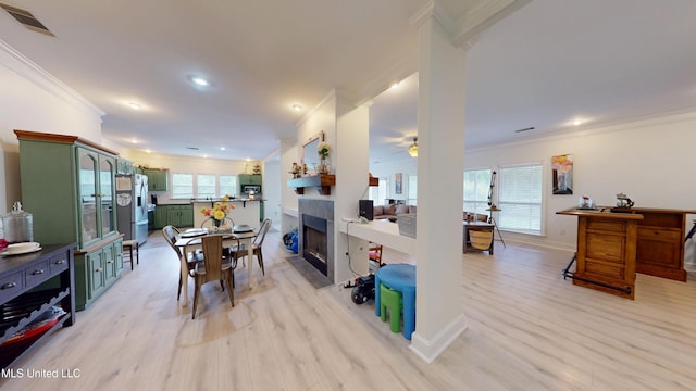dining space featuring ceiling fan, light wood-style floors, a tile fireplace, visible vents, and ornamental molding