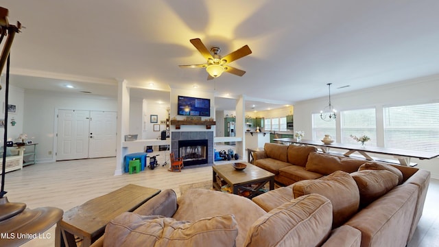 living area with crown molding, wood finished floors, baseboards, a tile fireplace, and ceiling fan with notable chandelier