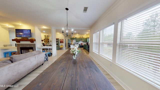 dining room featuring visible vents, a tile fireplace, a notable chandelier, light wood-style floors, and ornamental molding