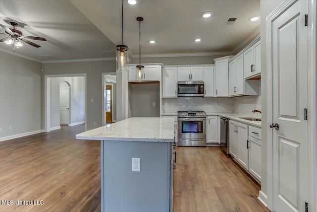 kitchen featuring wood finished floors, visible vents, appliances with stainless steel finishes, a center island, and crown molding