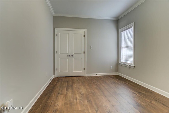 empty room with dark wood-type flooring, crown molding, and baseboards