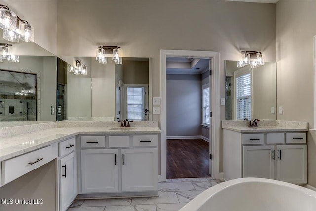 full bath with a freestanding tub, two vanities, a sink, baseboards, and marble finish floor