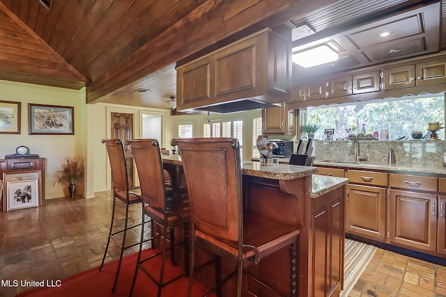 kitchen with lofted ceiling, light stone counters, a kitchen island, a kitchen breakfast bar, and sink