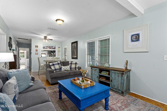 living room featuring a wealth of natural light, beam ceiling, wood-type flooring, and ceiling fan