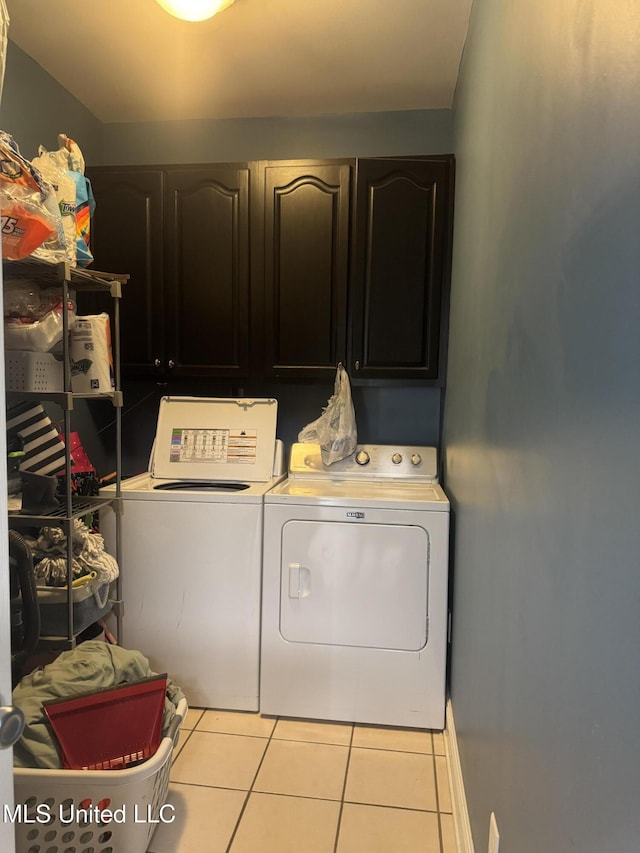 washroom featuring cabinet space, washer and dryer, light tile patterned floors, and baseboards
