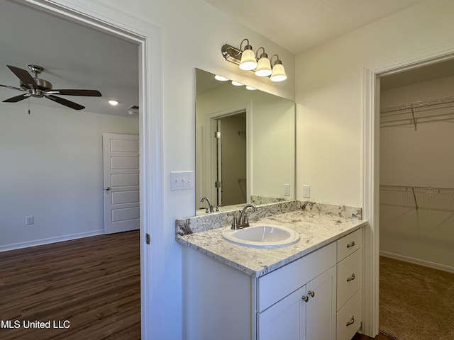 bathroom featuring baseboards, a ceiling fan, wood finished floors, a walk in closet, and vanity