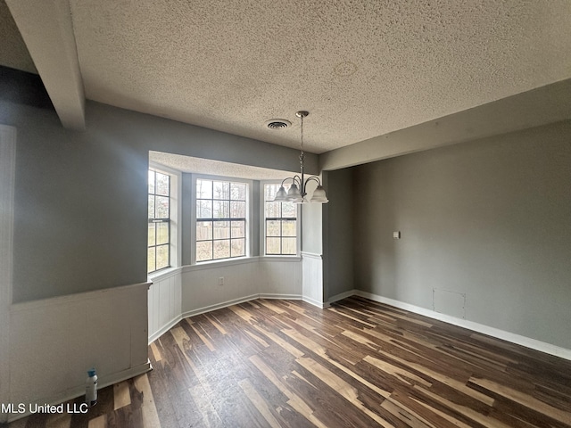 unfurnished dining area featuring an inviting chandelier, dark hardwood / wood-style floors, and a textured ceiling