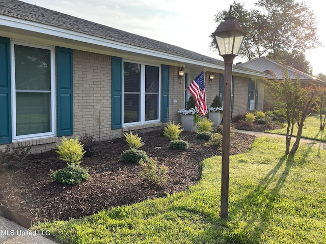 single story home with a shingled roof, a front yard, and brick siding