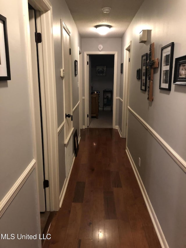 corridor featuring baseboards and dark wood-type flooring