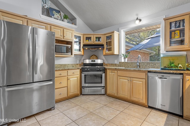 kitchen featuring light stone countertops, sink, stainless steel appliances, vaulted ceiling, and light tile patterned floors