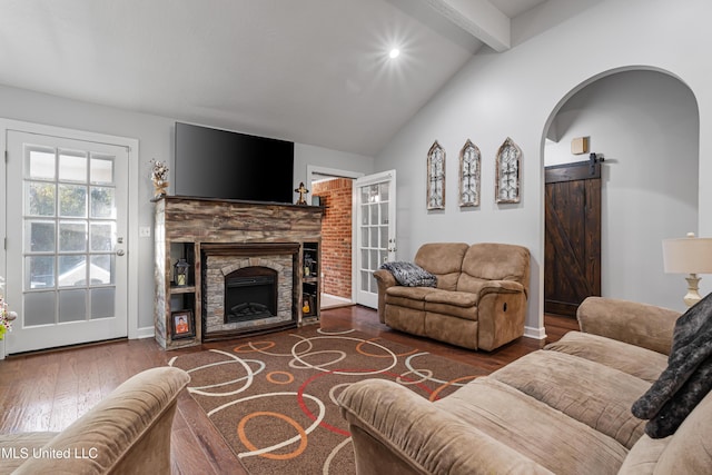 living room featuring a barn door, vaulted ceiling with beams, a stone fireplace, and hardwood / wood-style flooring