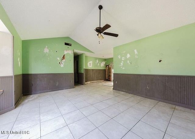 empty room featuring vaulted ceiling, ceiling fan, wooden walls, and light tile patterned flooring