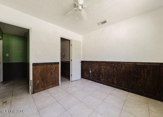 spare room featuring light tile patterned floors, a textured ceiling, ceiling fan, and wood walls