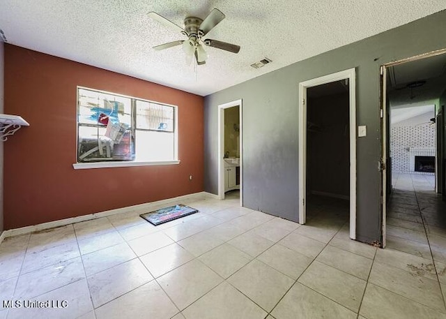 tiled empty room with a tile fireplace, a textured ceiling, and ceiling fan