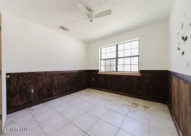 spare room with a textured ceiling, ceiling fan, wooden walls, and light tile patterned flooring