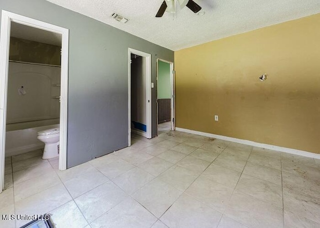 unfurnished bedroom with ensuite bathroom, a textured ceiling, ceiling fan, a spacious closet, and light tile patterned flooring