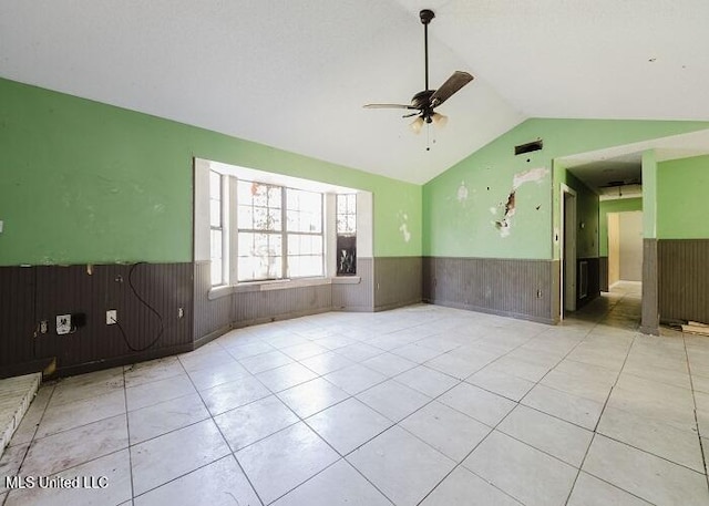 spare room featuring light tile patterned flooring, vaulted ceiling, ceiling fan, and wood walls