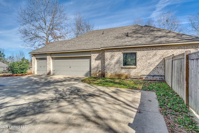 view of side of property featuring an attached garage, brick siding, fence, driveway, and roof with shingles