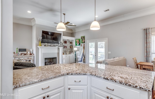 kitchen featuring light stone counters, crown molding, a fireplace, open floor plan, and white cabinetry