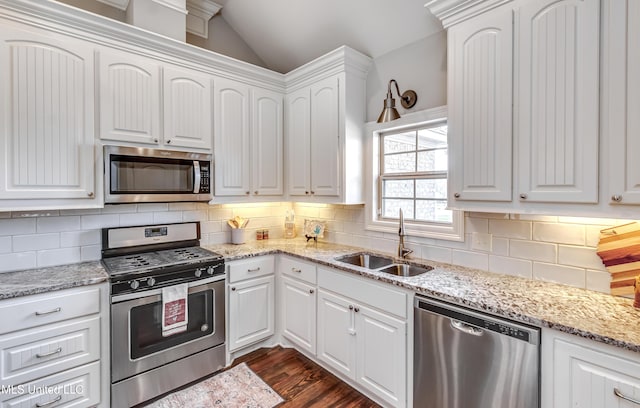 kitchen with appliances with stainless steel finishes, lofted ceiling, white cabinets, and a sink