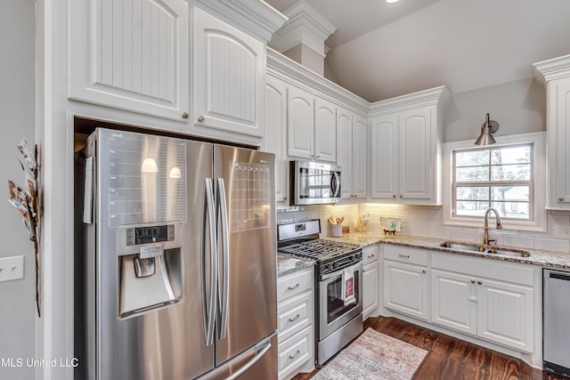 kitchen featuring stainless steel appliances, backsplash, white cabinets, a sink, and light stone countertops