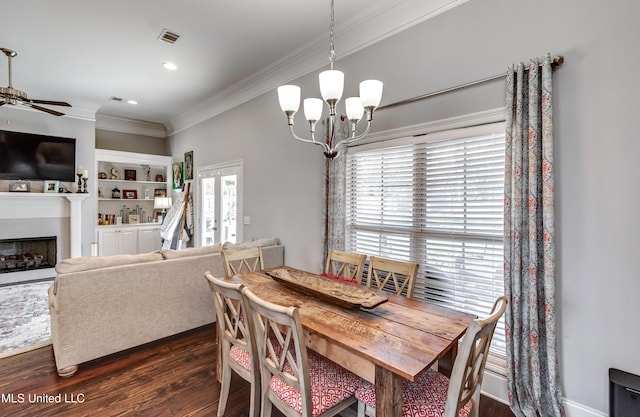 dining room with ceiling fan with notable chandelier, dark wood-style flooring, a fireplace, visible vents, and ornamental molding