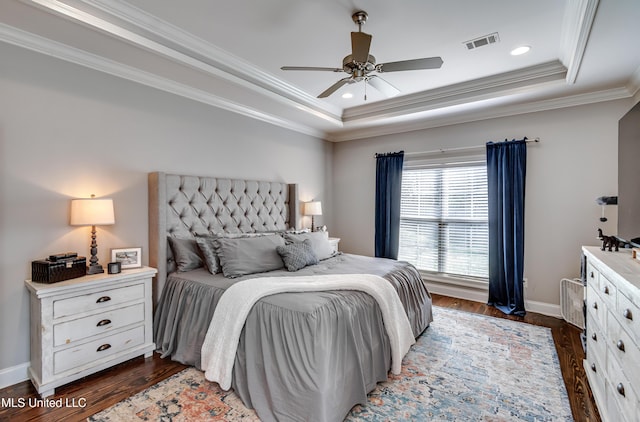 bedroom featuring visible vents, baseboards, ornamental molding, a tray ceiling, and dark wood finished floors