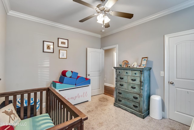 carpeted bedroom featuring a crib, ornamental molding, and a ceiling fan