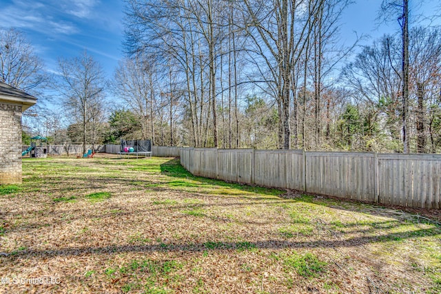 view of yard with a trampoline, a fenced backyard, and a playground