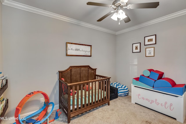 carpeted bedroom featuring ornamental molding, a crib, and a ceiling fan