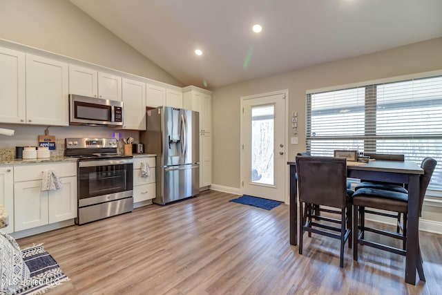 kitchen with appliances with stainless steel finishes, lofted ceiling, white cabinets, and light wood-style floors