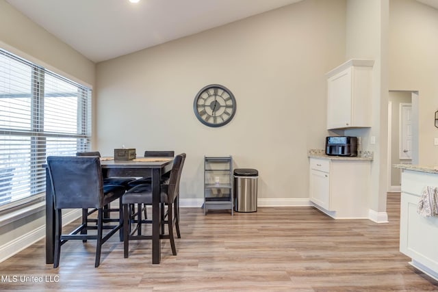 dining space featuring baseboards, vaulted ceiling, and light wood finished floors