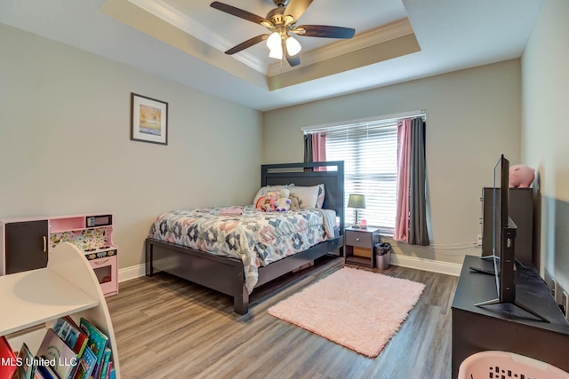 bedroom with ceiling fan, wood finished floors, baseboards, ornamental molding, and a tray ceiling