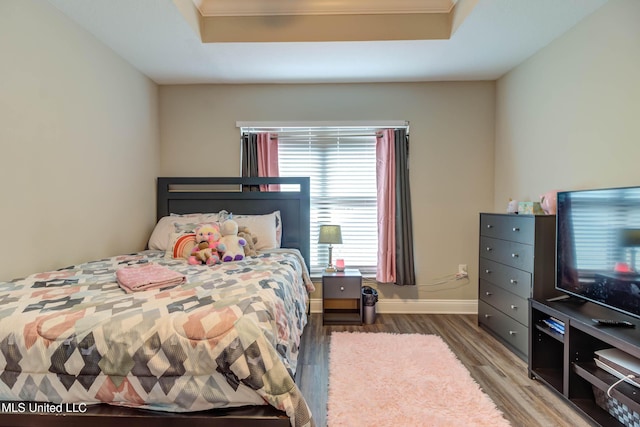 bedroom featuring a raised ceiling, wood finished floors, and baseboards