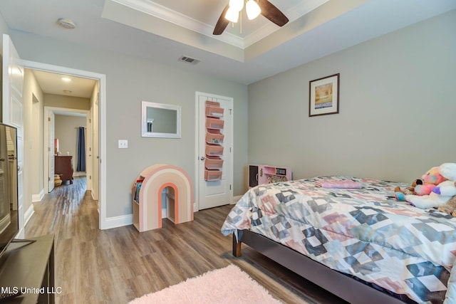 bedroom with crown molding, a raised ceiling, visible vents, wood finished floors, and baseboards