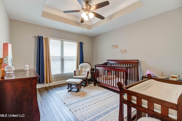 bedroom with baseboards, a raised ceiling, a ceiling fan, wood finished floors, and crown molding