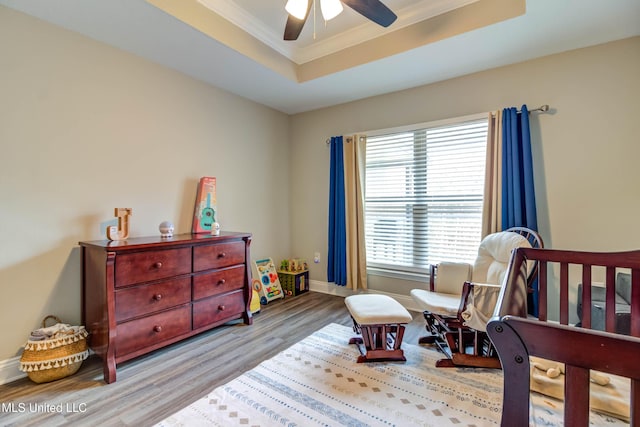 bedroom featuring ceiling fan, wood finished floors, baseboards, ornamental molding, and a raised ceiling