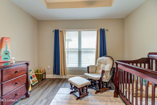 bedroom with a crib, baseboards, a raised ceiling, and wood finished floors