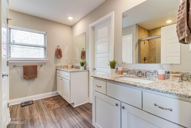 bathroom featuring wood finished floors, two vanities, a sink, baseboards, and a stall shower