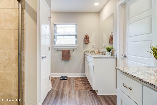 full bath featuring recessed lighting, vanity, wood finished floors, tiled shower, and baseboards