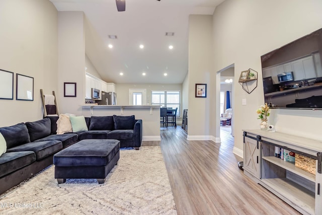 living room with high vaulted ceiling, light wood-type flooring, visible vents, and baseboards