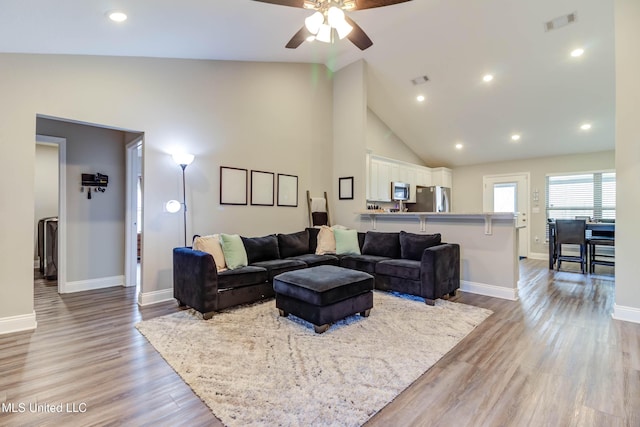 living room with high vaulted ceiling, light wood-type flooring, visible vents, and baseboards