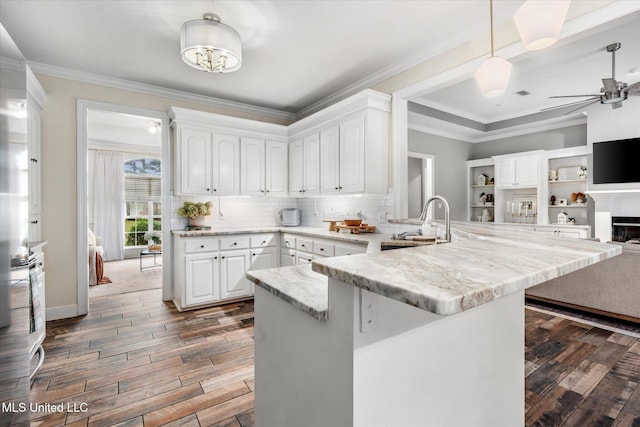 kitchen featuring kitchen peninsula, light stone countertops, sink, dark hardwood / wood-style floors, and white cabinetry