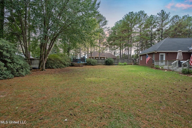 yard at dusk with a trampoline and a wooden deck