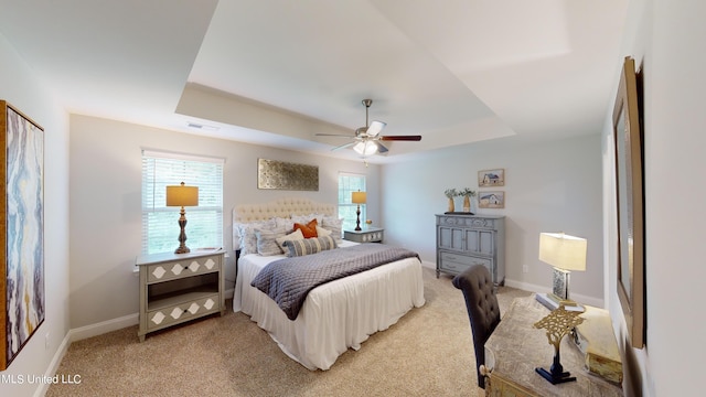 bedroom with a raised ceiling, light carpet, and ceiling fan