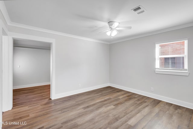 spare room with crown molding, wood finished floors, visible vents, and baseboards