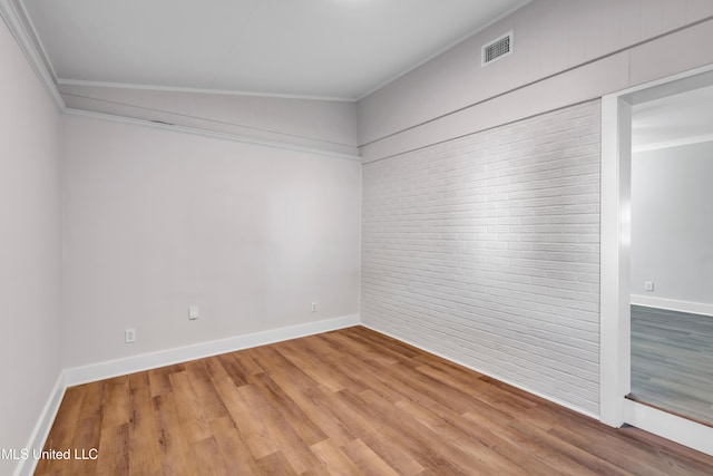 spare room featuring visible vents, brick wall, baseboards, ornamental molding, and light wood-style flooring