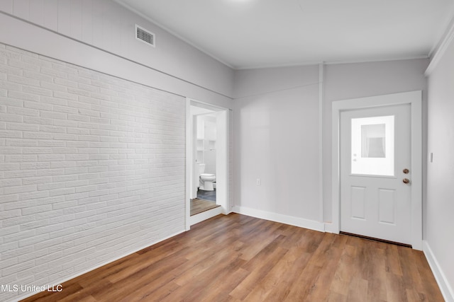 foyer with visible vents, brick wall, crown molding, baseboards, and wood finished floors