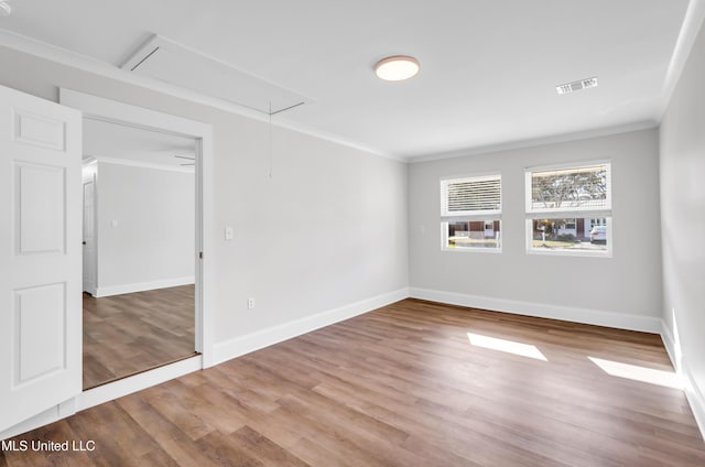 spare room featuring attic access, wood finished floors, visible vents, and ornamental molding