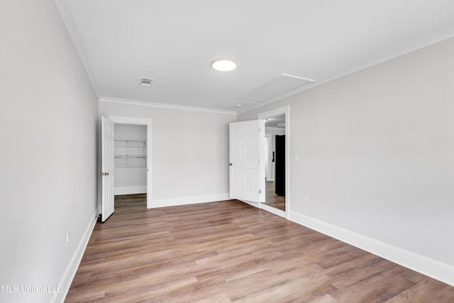 empty room with visible vents, crown molding, attic access, and light wood-type flooring